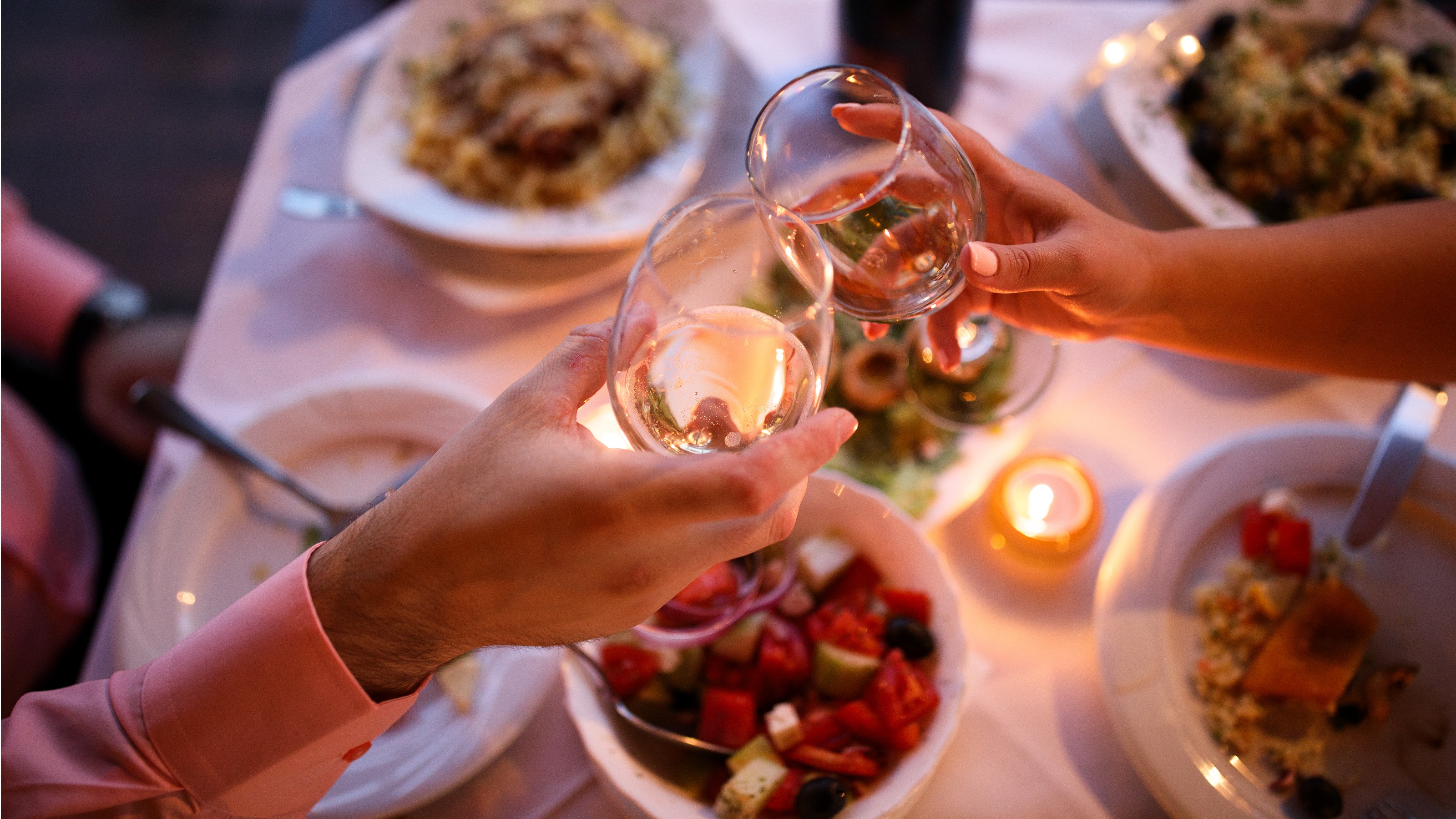 A couple tap wineglasses over dinner at a restaurant.