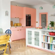 pink kitchen cabinets with a white kitchen island, matching pink framed glass door, herringbone wood flooring, and a dining table and chairs