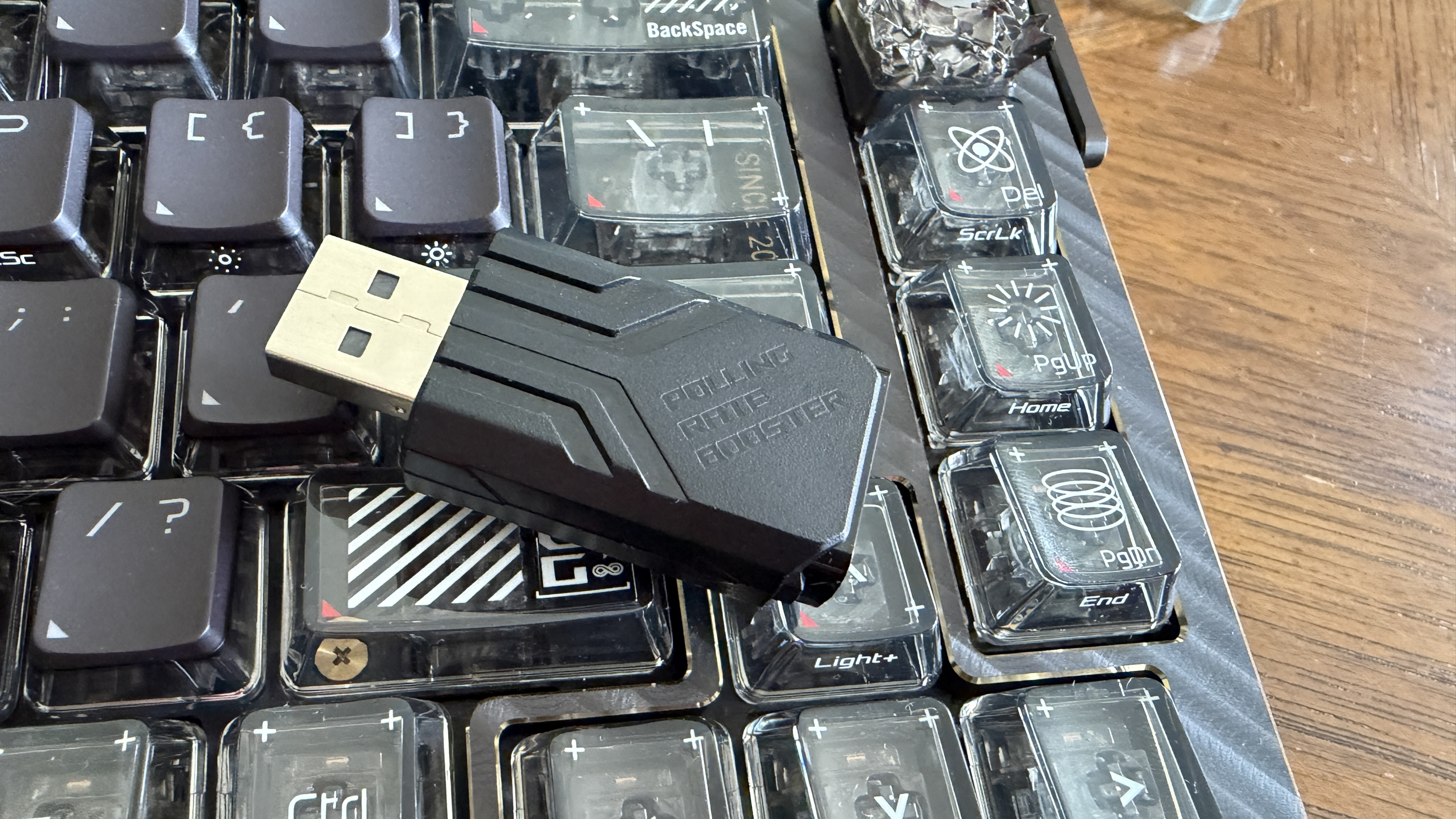 A black USB device labeled "Polling Rate Booster" rests on a mechanical keyboard with translucent keycaps.