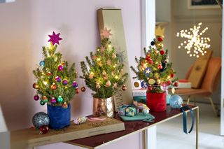 A hallway with three mini Christmas trees on console table