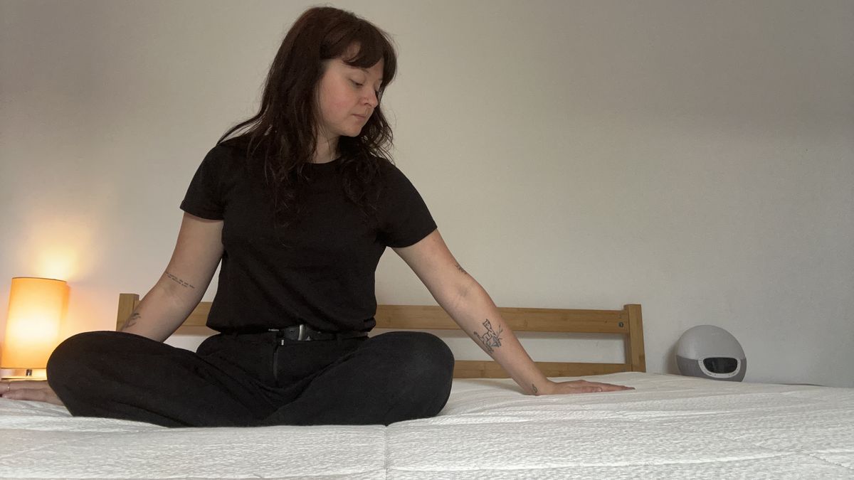 A Tom's Guide mattress tester sitting on and lying on the Awara Classic mattress