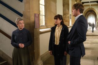 Marion Goddard (Emma Fielding) stands in the school corridor at the foot of a staircase, speaking to DS Esther Williams (Zahra Ahmadi) and DI Humphrey Goodman (Kris Marshall)