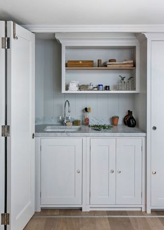 A folding white door separating off an all white laundry room area with gray marble countertops and open shelving.