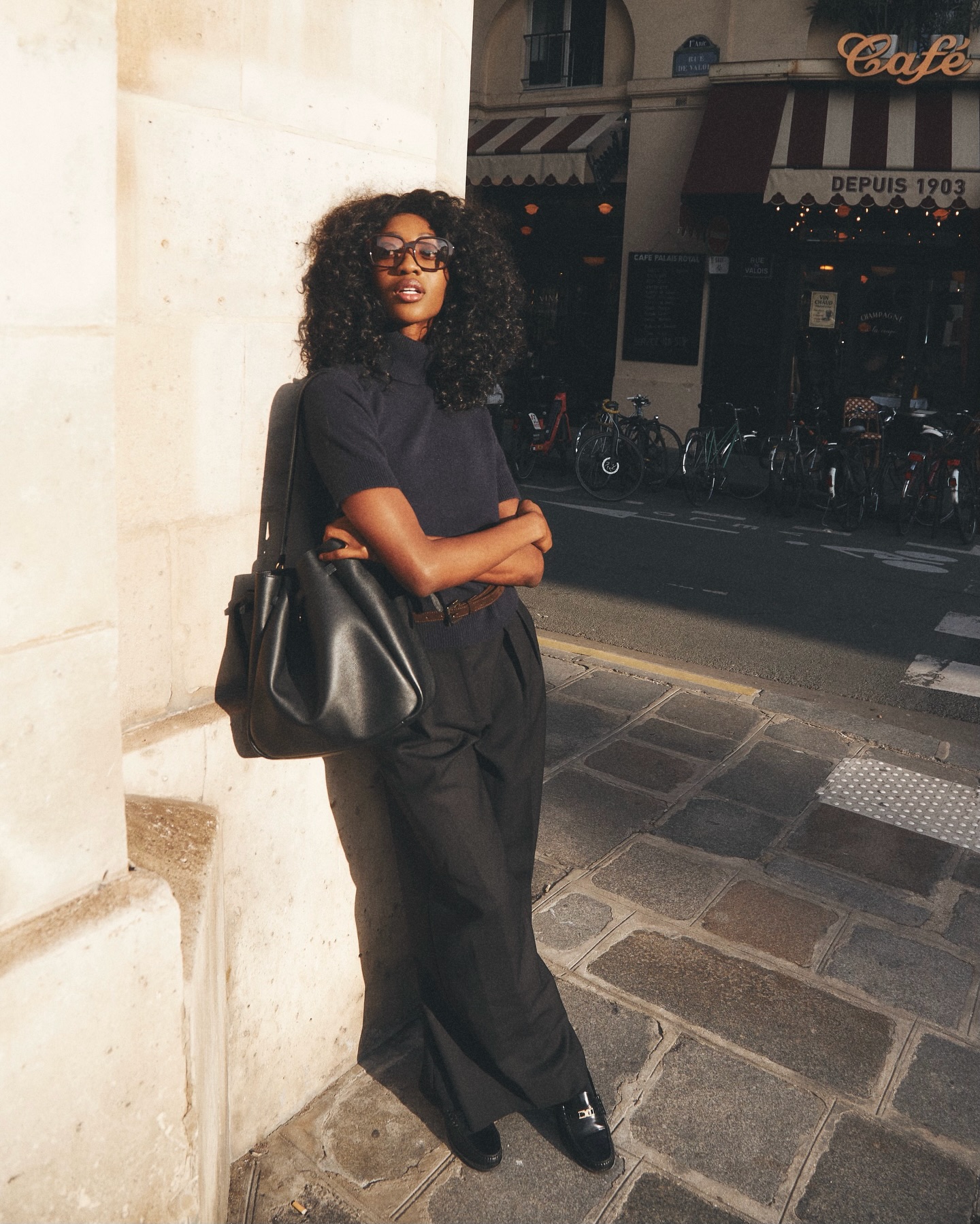An image of an influencer in Paris wearing a navy short-sleeve, high-neck knit with tailored black trousers and black loafers, carrying a black leather tote
