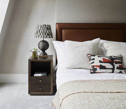 A neutral bedroom with a patterned lampshade and textured cushions and a fluffy throw