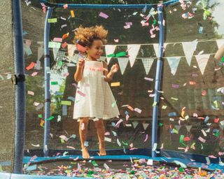 Little girl jumping on a trampoline at a party with confetti and bunting