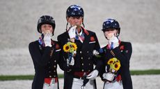 British dressage team (left to right: Charlotte Dujardin, Carl Hester, Lottie Fry) kiss their bronze medals while standing on the podium in Tokyo