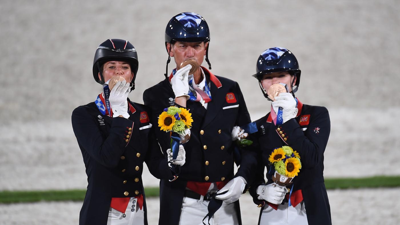 British dressage team (left to right: Charlotte Dujardin, Carl Hester, Lottie Fry) kiss their bronze medals while standing on the podium in Tokyo