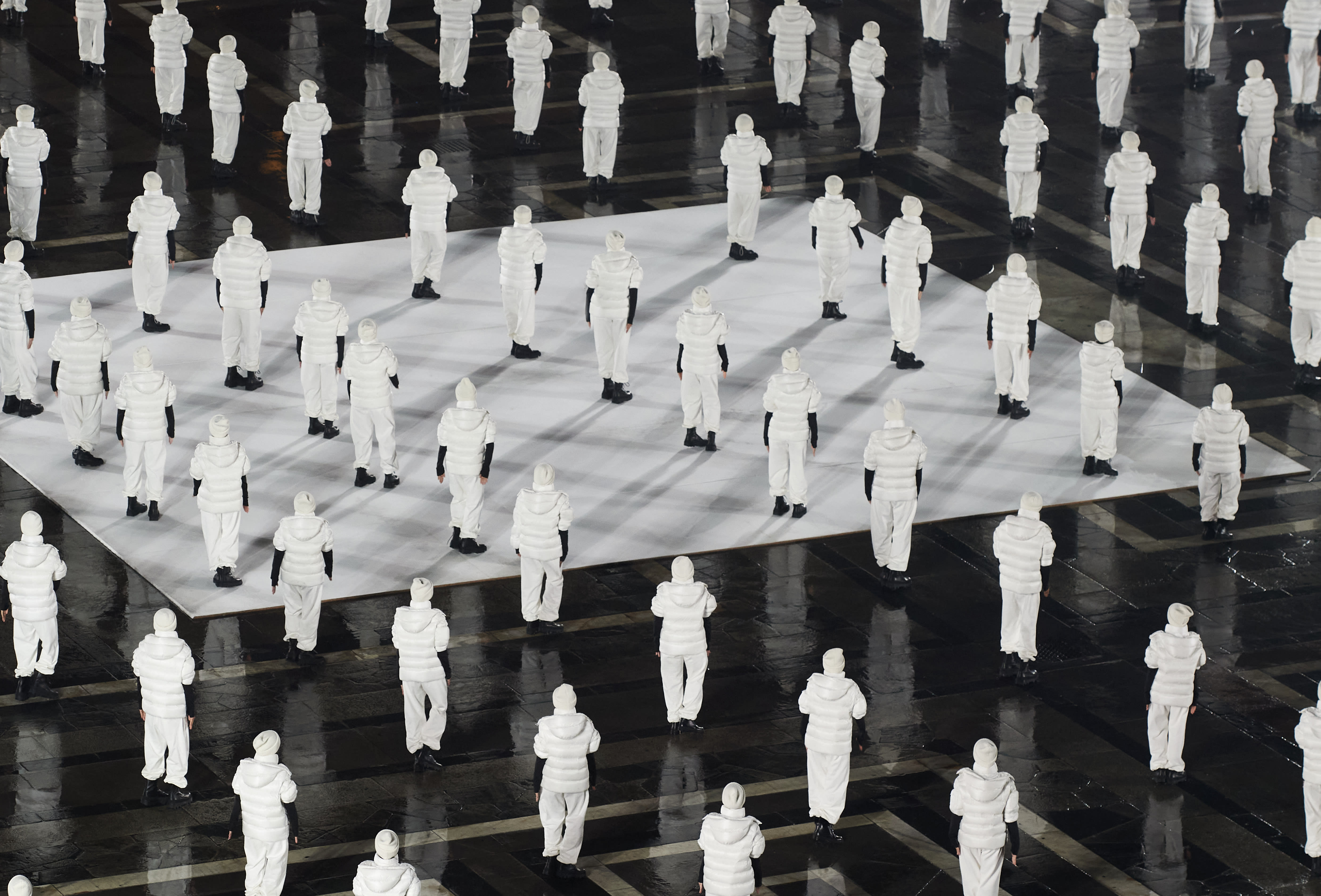 An overview of many people standing in rows all wearing white jackets, white pants and black boots.