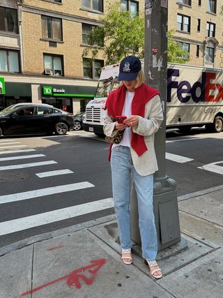 Lara Mead, De Varley, Vestindo Um Blazer Bege E Jeans Com Um Suéter De Cashmere Vermelho Sobre Os Ombros.