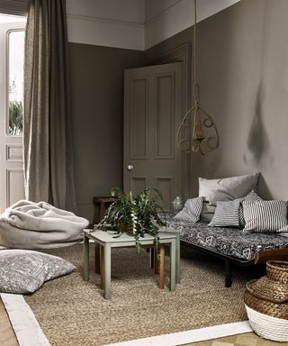 A living room paint color idea by Annie Sloan using Wall Paint in French Linen Old White – a Moroccan-style living room with pouffes, ottomans, plants and a hanging planter, in gray and wood tones