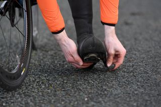 Image shows a rider putting on overshoes to avoid cold feet while cycling.