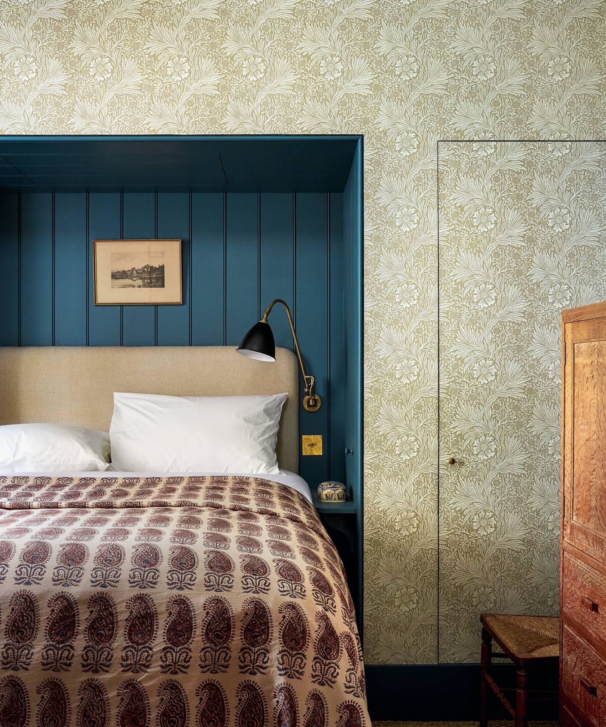 Vintage bedroom with wallpapered walls and a blue panelled nook with bed and vintage throw