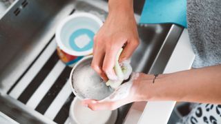 A person washing a stainless steel cat bowl