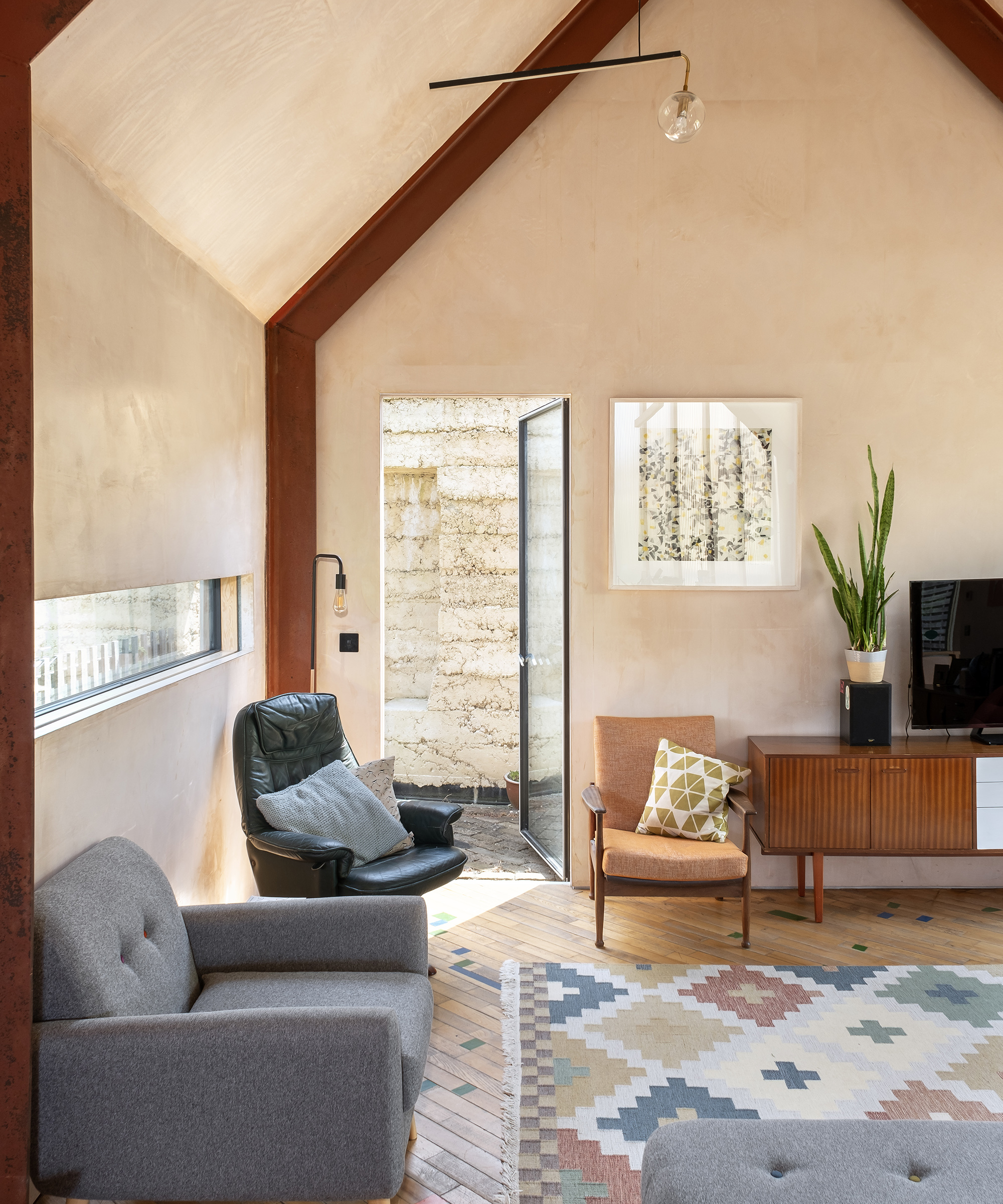 A cosy living area in a self build home. There is a large Navajo rug on the wooden flooring and a long, narrow window on the left hand wall letting in extra light