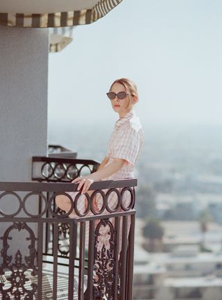 Actress Shira Haas poses for a portrait in support of her latest film Captain America: Brave New World wearing a pink and white gingham shirtdress, black ankle boots, and black sunglasses.