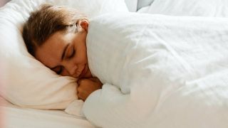 Young woman all tucked in under the quilt in bed