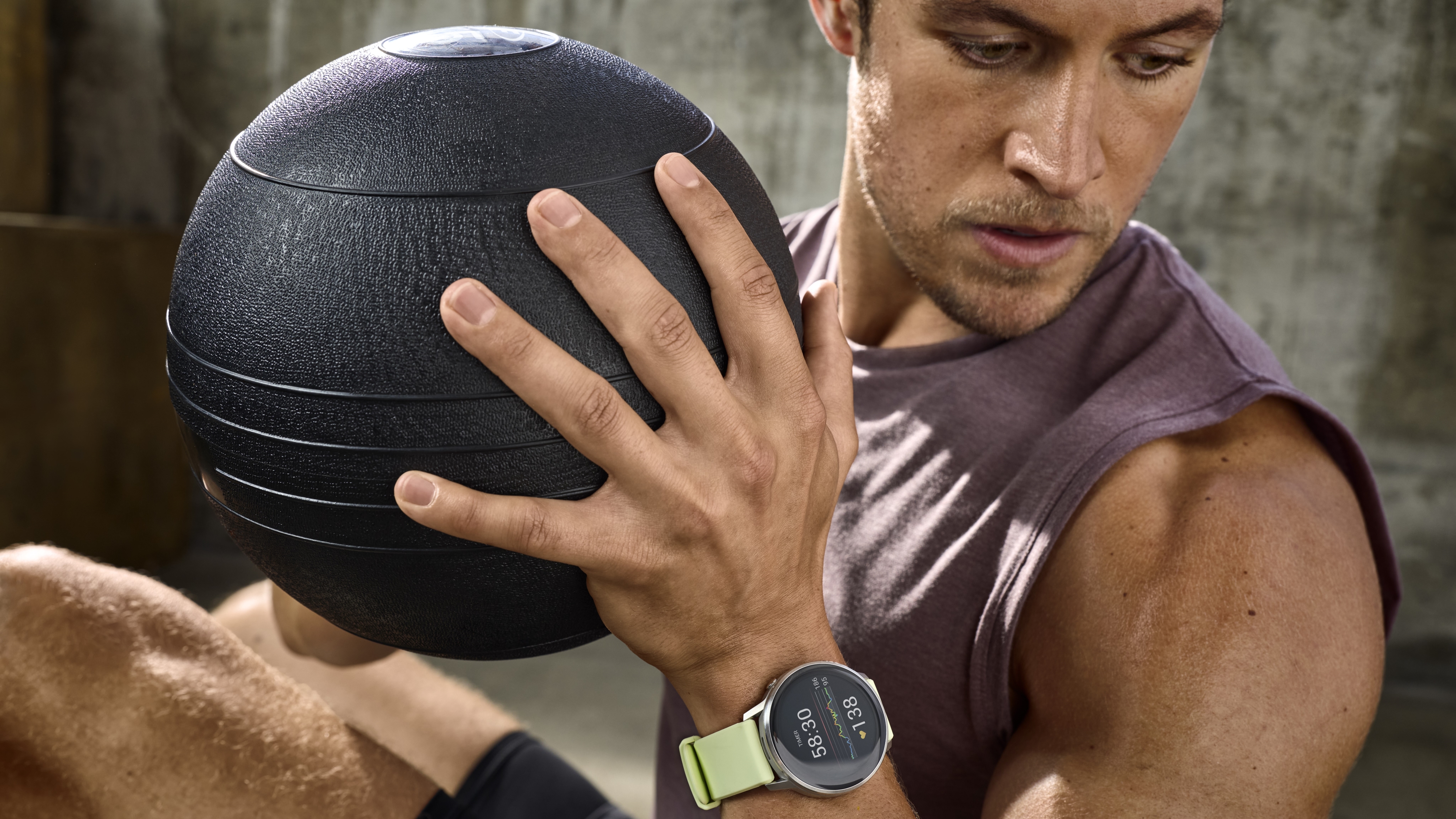 A photo of the Garmin Venu 4 on a man&#039;s wrist as he works out with an exercise ball.