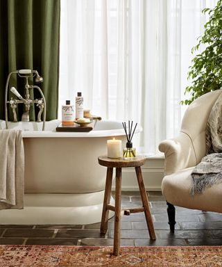 Freestanding bathtub with cream upholstered chair and heavy green draped curtains