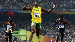 Three men sprint down a race track. The man in the middle has his arms outstretched and his mouth open in a yell or smile