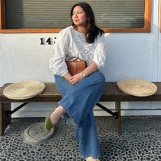 marina wears embroidered longsleeve white top, jeans, chartreuse green satin mules and a brown handbag while sitting 
