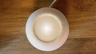 White Homepod Mini on a flat wooden surface.