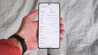 OnePlus 13 phone held in a hand showing the phone specifications on its screen