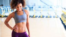 Woman in exercise clothing showing off her toned abs after completing a 30-day trim waist challenge