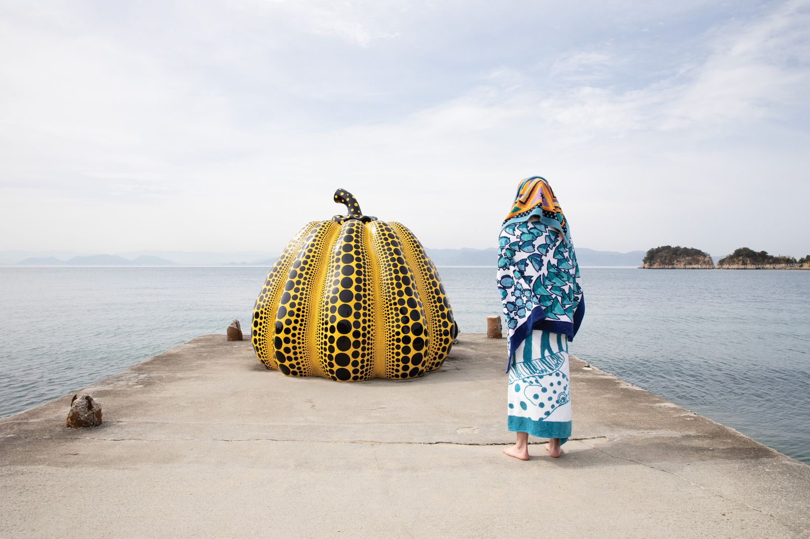Yayoi Kusamma pumpkin artwork on jetty, and person covered in beach towels