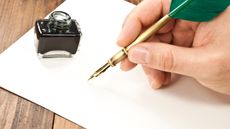 A man's hand grips a fountain pen, preparing to write on a piece of paper.