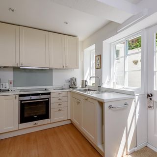 a light and airy kitchen with with wooden floor and cream cabinets, with sink in front of windows