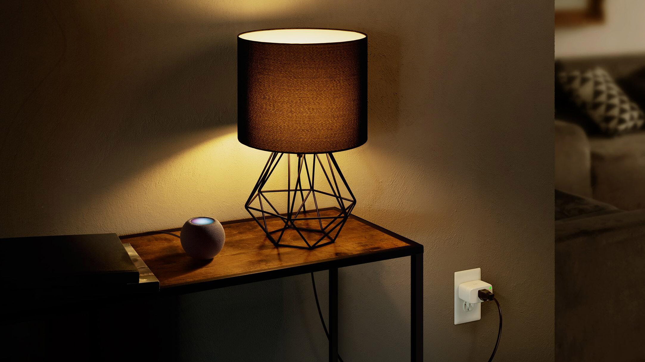 Eve Energy smart plug in an electrical socket with a lamp and HomePod Mini on a table above