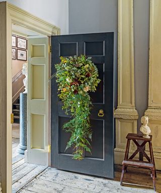 Thanksgiving wreath ideas with large pine and foliage wreath on a black indoor door, with fern tail draping to the floor