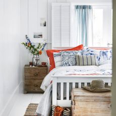 White painted bedroom and window with white bedframe and decorative cushions, bedside table with flowers