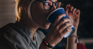 A blonde woman with glasses sipping coffee with a black Samsung fitness tracker on her wrist
