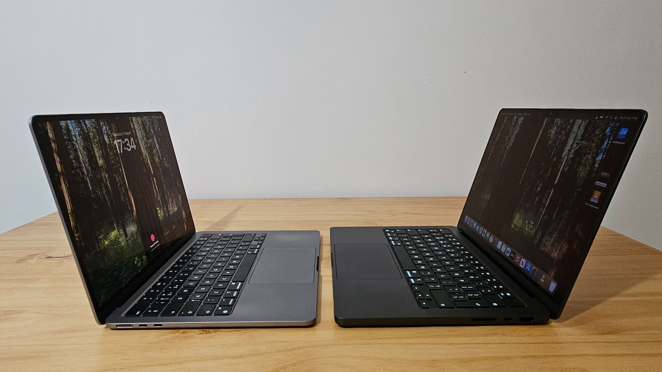 Two opened MacBooks facing each other on a wooden table.