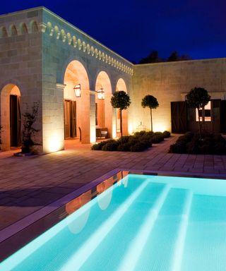 A backyard pool with graduated steps lit with LED lighting at night time