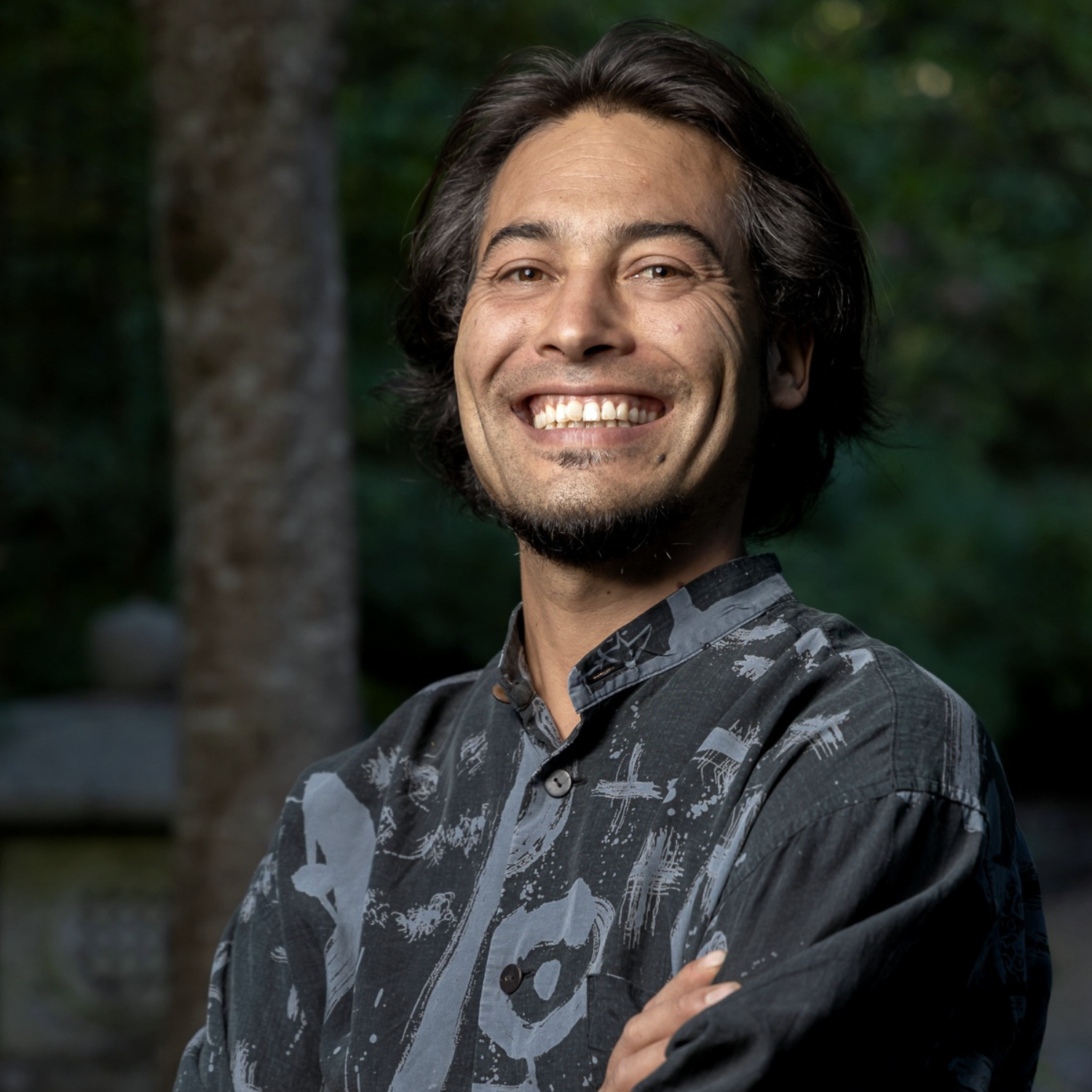 A headshot of a man with sort black hair and a stubble in a collared shirt with paint swirl designs