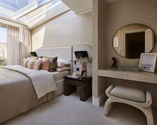 neutral bedroom with large skylight, shimmer effect wallpaper, bed with white oversized headboard and dressing table