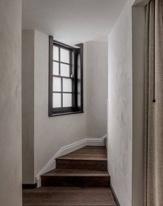 A staircase with white walls, wooden flooring and a window.