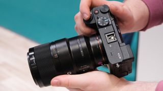 Sony FE 90mm lens attached to a Sony camera and held in a pair of hands