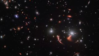 An deep-field image of numerous galaxies and gravitational lensing effects.