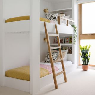 A girls' bedroom with twin bunk bed, wooden ladder, and coordinated pink, mustard and white bedding