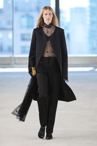 Model at Toteme Spring 2025 show wearing sheer top under black coat and black pants