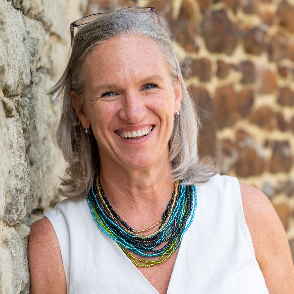 female with shoulder length grey wearing white v neck sleeveless top and beaded necklaces