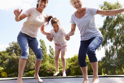 Grandmother, Granddaughter And Mother Bouncing On Trampoline