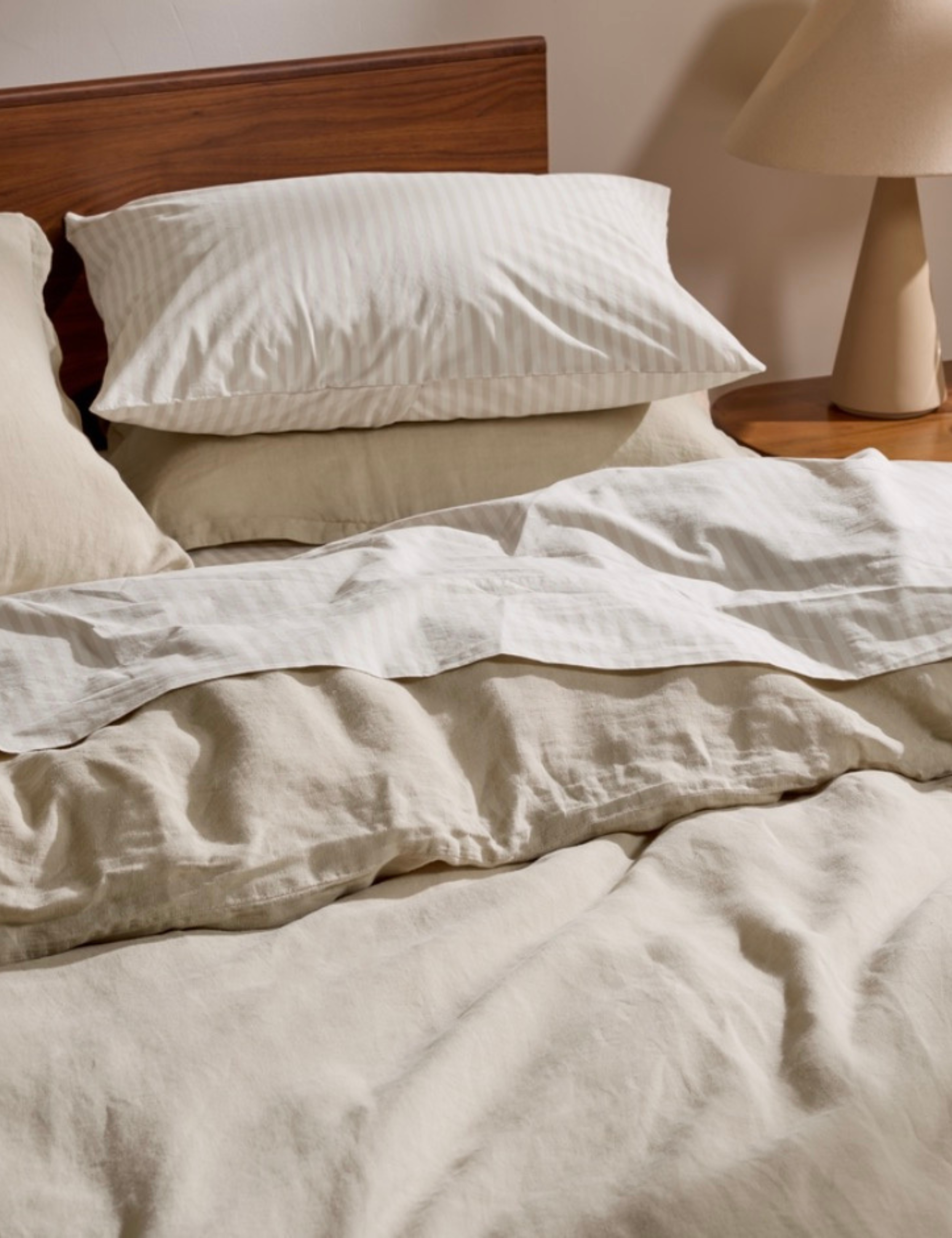 Solid beige and striped bed sheets pictured in a neutral bedroom