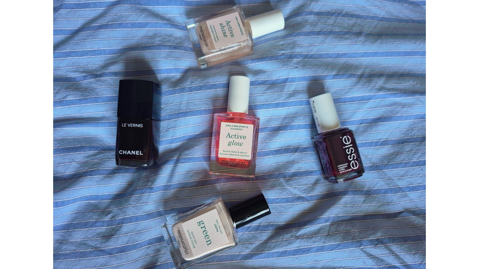 Nail polishes from essie, Manucurist and Chanel laying on blue pinstripe bedding
