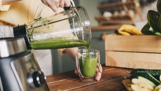 Woman's hands pouring spinach smoothie into a glass from a blender