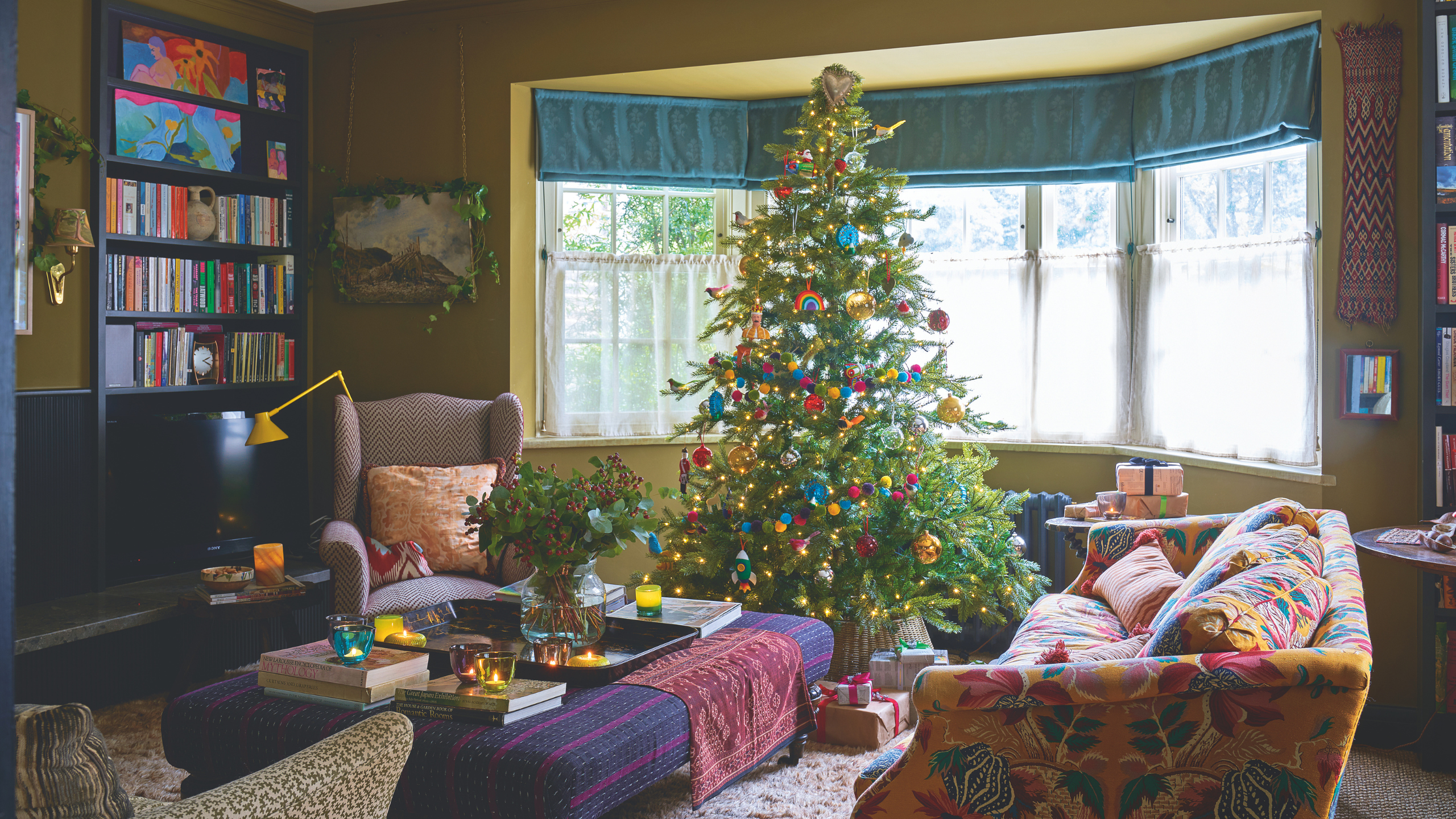 a nostalgic Christmas living room with a large tree decorated with colorful ornaments, a patterned couch, and an ottoman with a vase of flowers on top
